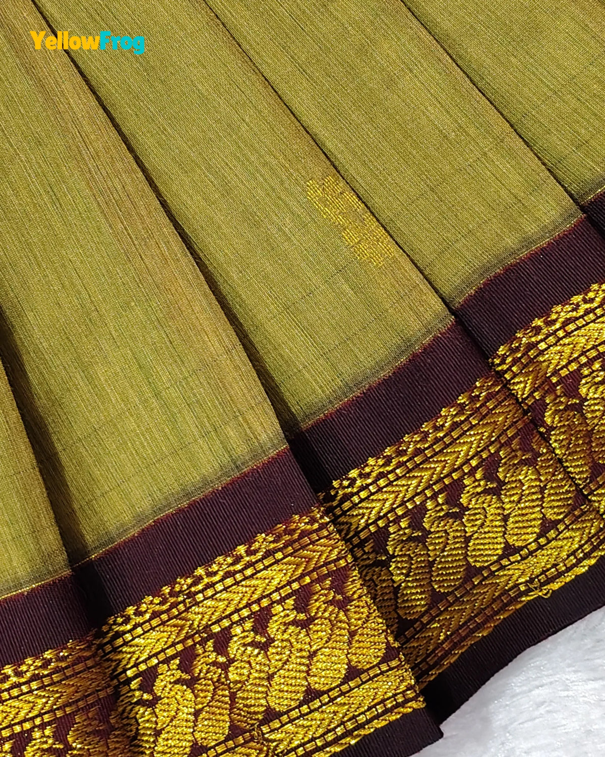 A close-up of a pleated olive green fabric, likely a sari, featuring a wide dark maroon border with an intricate gold woven floral and paisley pattern.