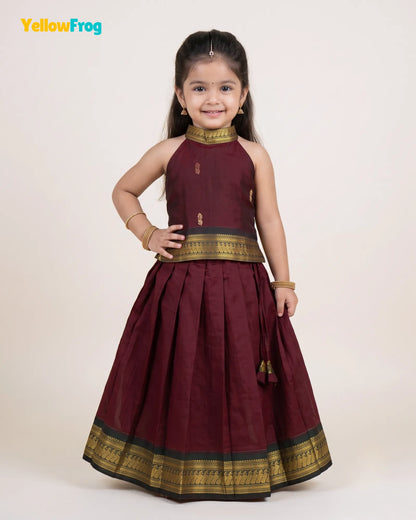 A young girl modeling a traditional Indian outfit consisting of a sleeveless maroon lehenga skirt with gold zari borders and a matching maroon and gold choli top, set against a plain cream background.