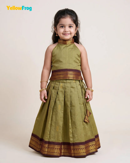 A young girl modeling a sleeveless olive green traditional dress with gold and maroon borders, standing against a plain beige studio background. The YellowFrog logo is visible in the top left corner.