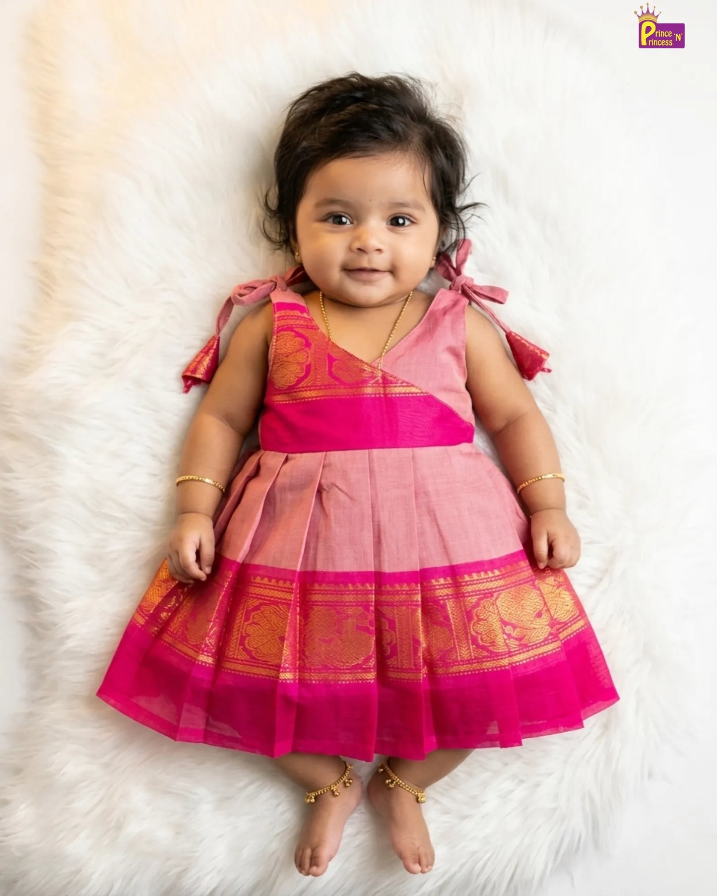 Baby wearing a pink traditional outfit on a white fur background