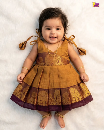 Baby wearing a mustard yellow and brown traditional dress on a white background
