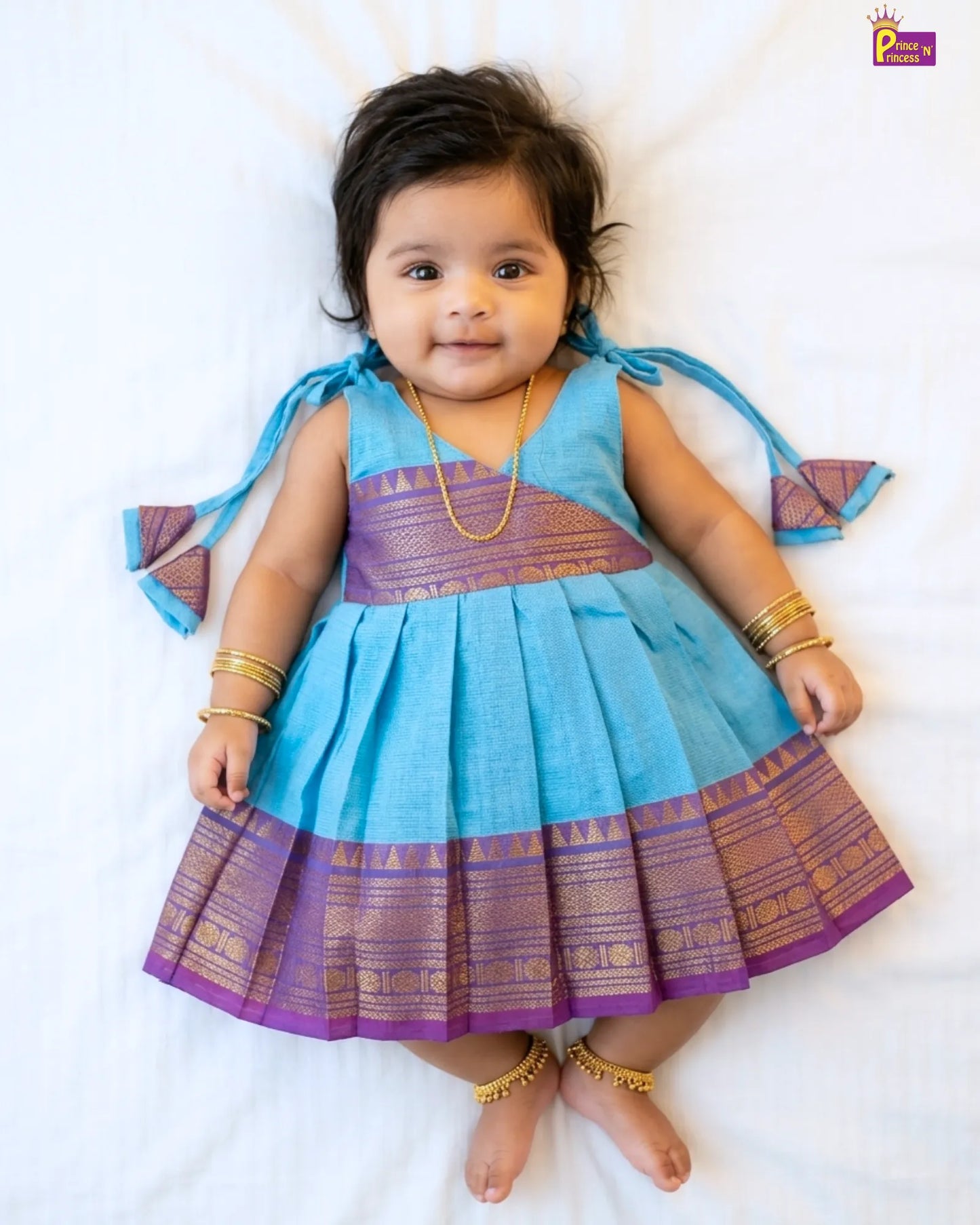 Baby wearing a blue and purple traditional outfit on a white background