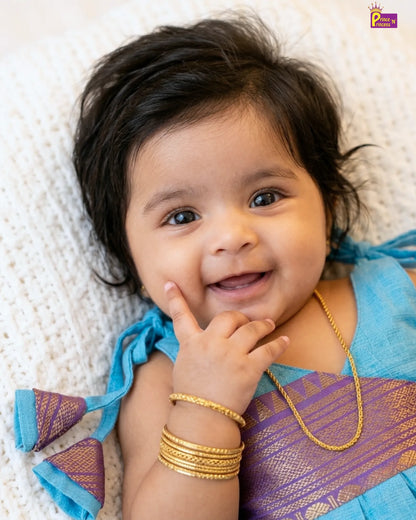 Baby wearing a blue and purple traditional outfit with gold jewelry on a white background