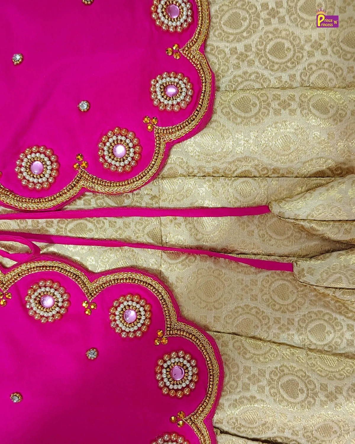 A close-up of a traditional Indian outfit fabric, featuring a bright pink dupatta with gold zari embroidery and mirror work, paired with a beige and gold brocade saree body.