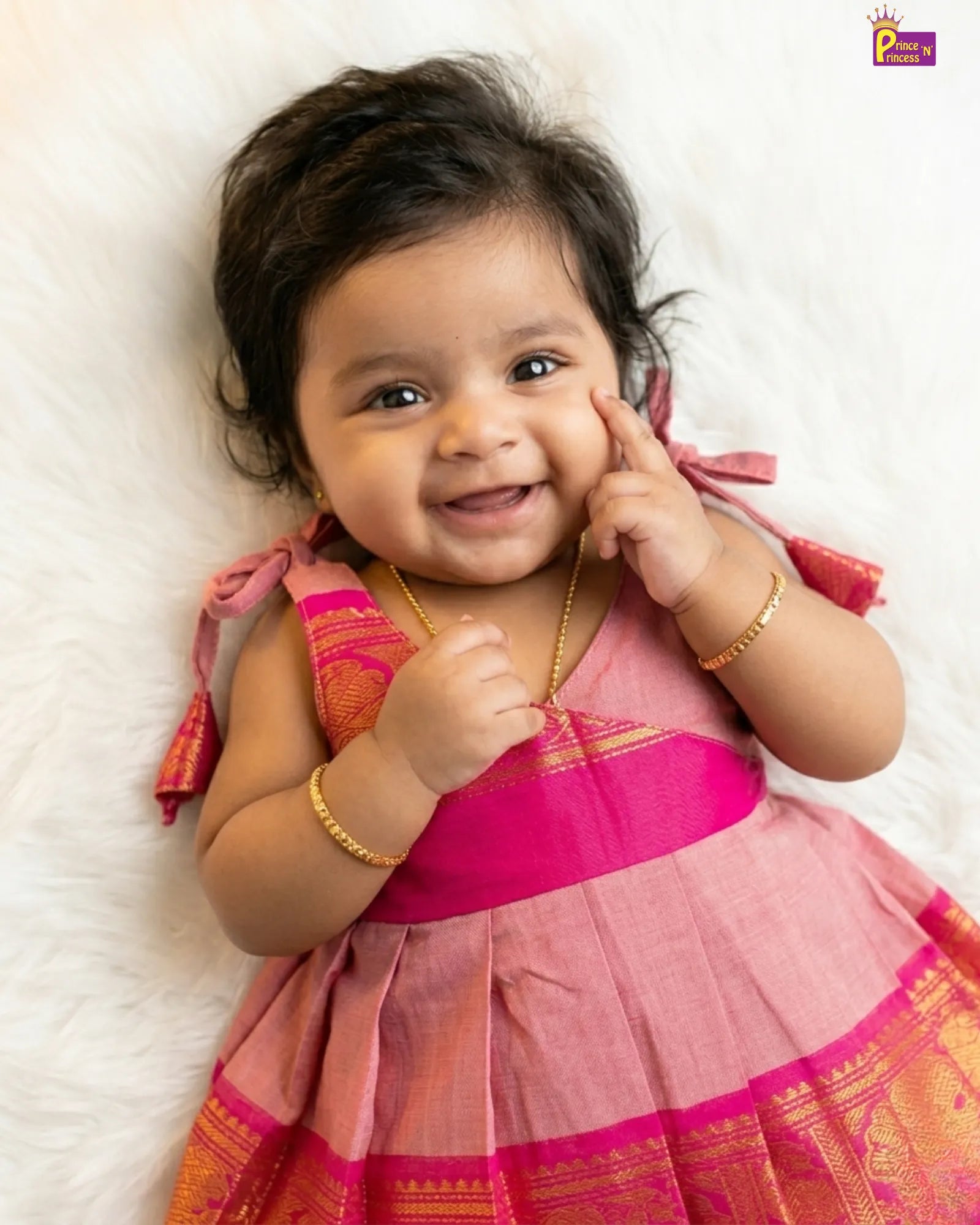 Baby in a pink traditional outfit lying on a white surface