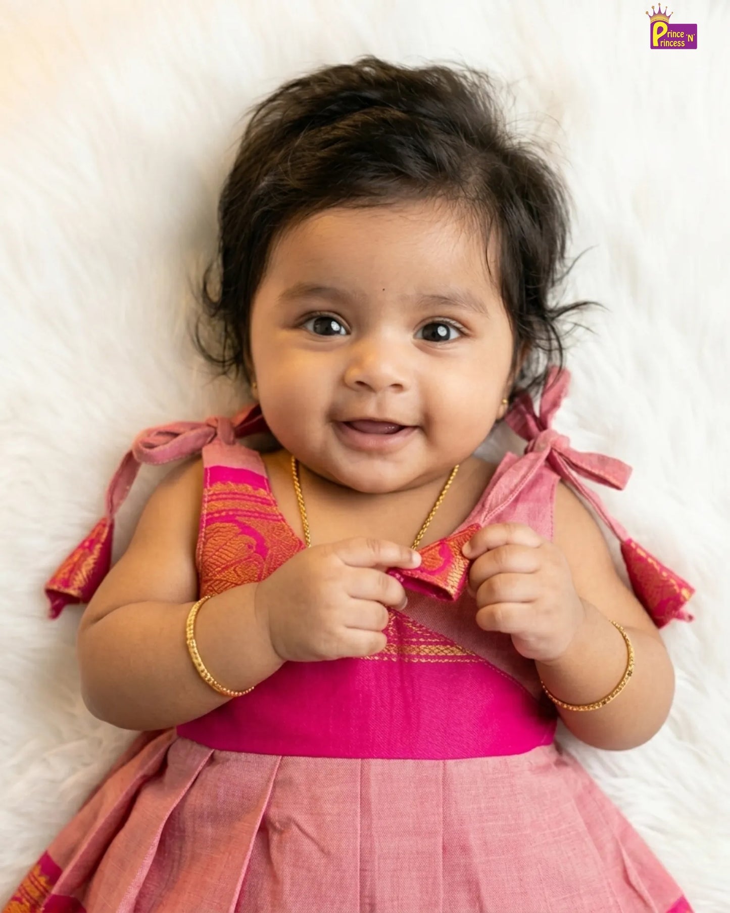 Baby in a pink traditional outfit lying on a white surface