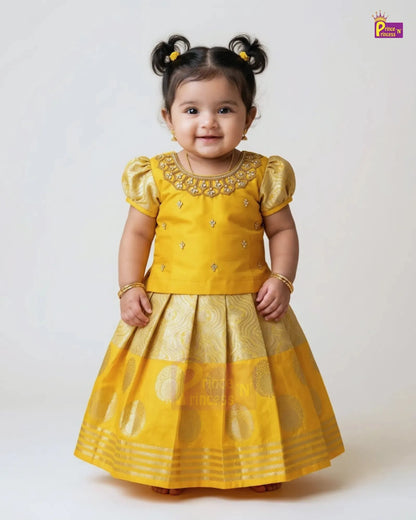 A toddler girl wearing a bright yellow traditional Indian dress with gold embroidery and a flared skirt, standing against a plain light background. The brand logo 'Padmini' is visible in the top right corner.