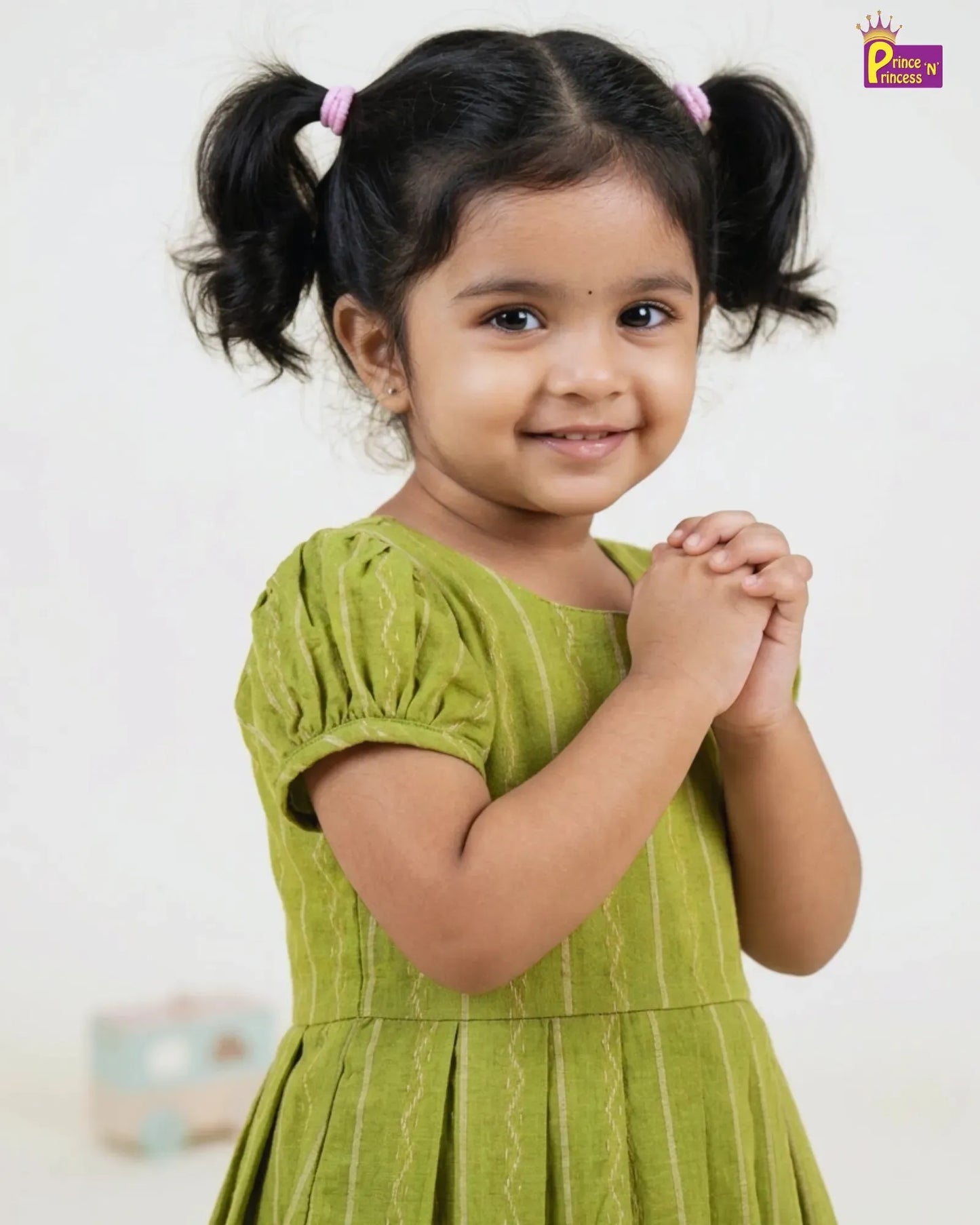 Young girl in a green dress with pigtails against a plain background