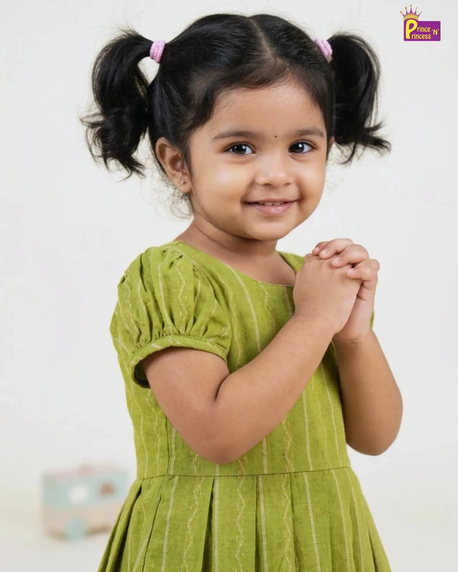Young girl in a green dress with pigtails against a plain background