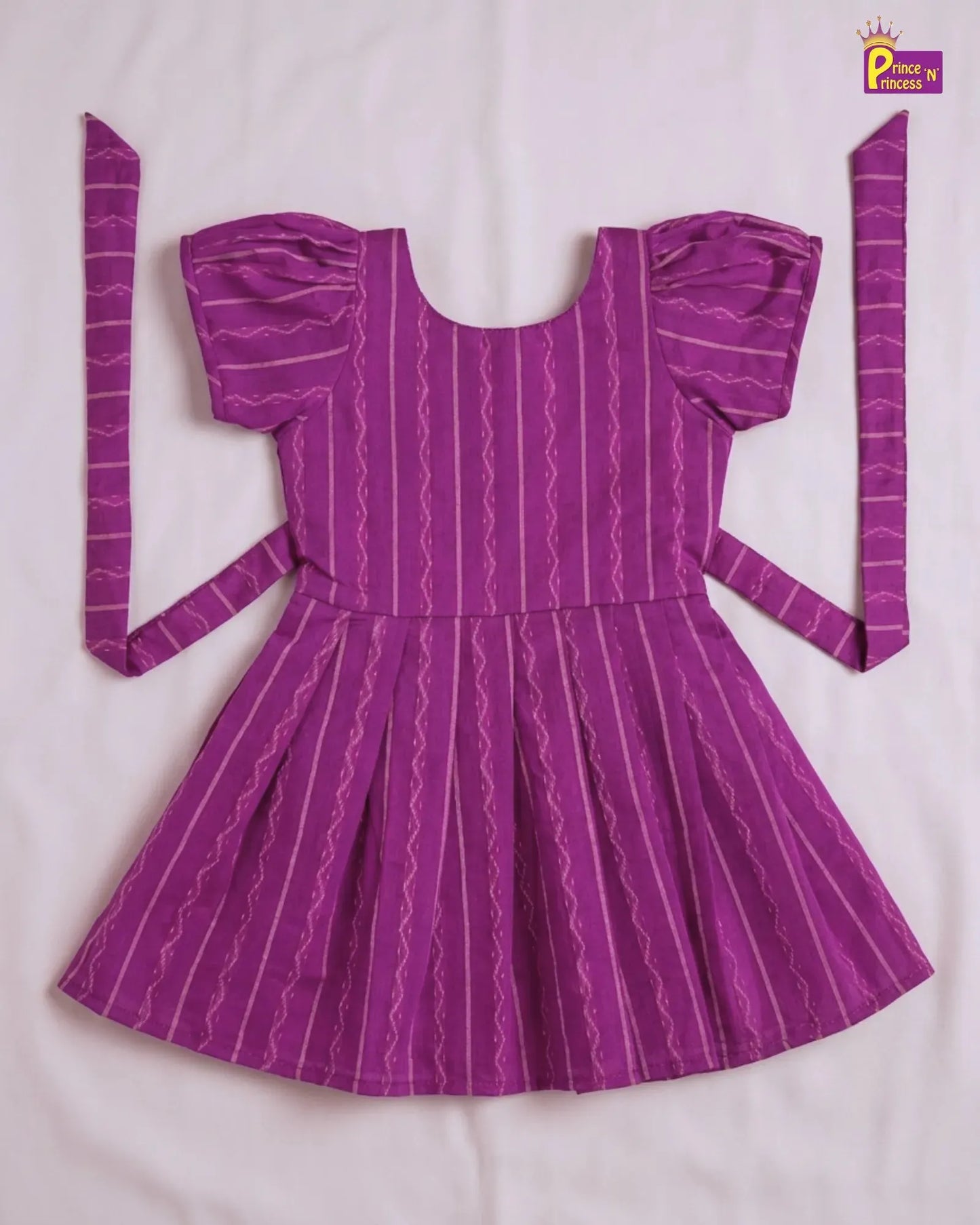 A purple short-sleeve dress with vertical wavy stripes, laid flat on a white fabric background. The dress features puffed short sleeves, a square neckline, a pleated skirt, and matching tie straps on the sides.