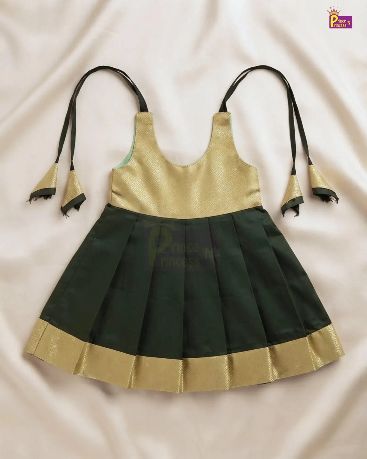 A sleeveless traditional-style dress with a metallic gold upper bodice and a dark green pleated skirt, laid flat on a light beige fabric background. The dress has thin black shoulder ties with gold bell-shaped ends and a gold border along the skirt hem.