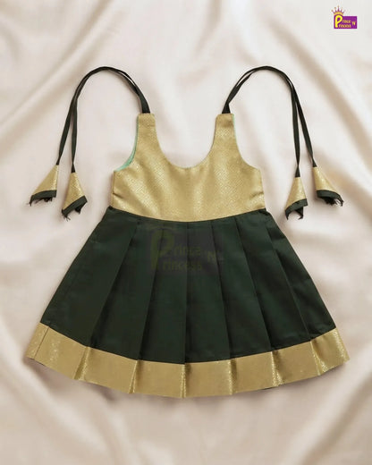 A sleeveless traditional-style dress with a metallic gold upper bodice and a dark green pleated skirt, laid flat on a light beige fabric background. The dress has thin black shoulder ties with gold bell-shaped ends and a gold border along the skirt hem.