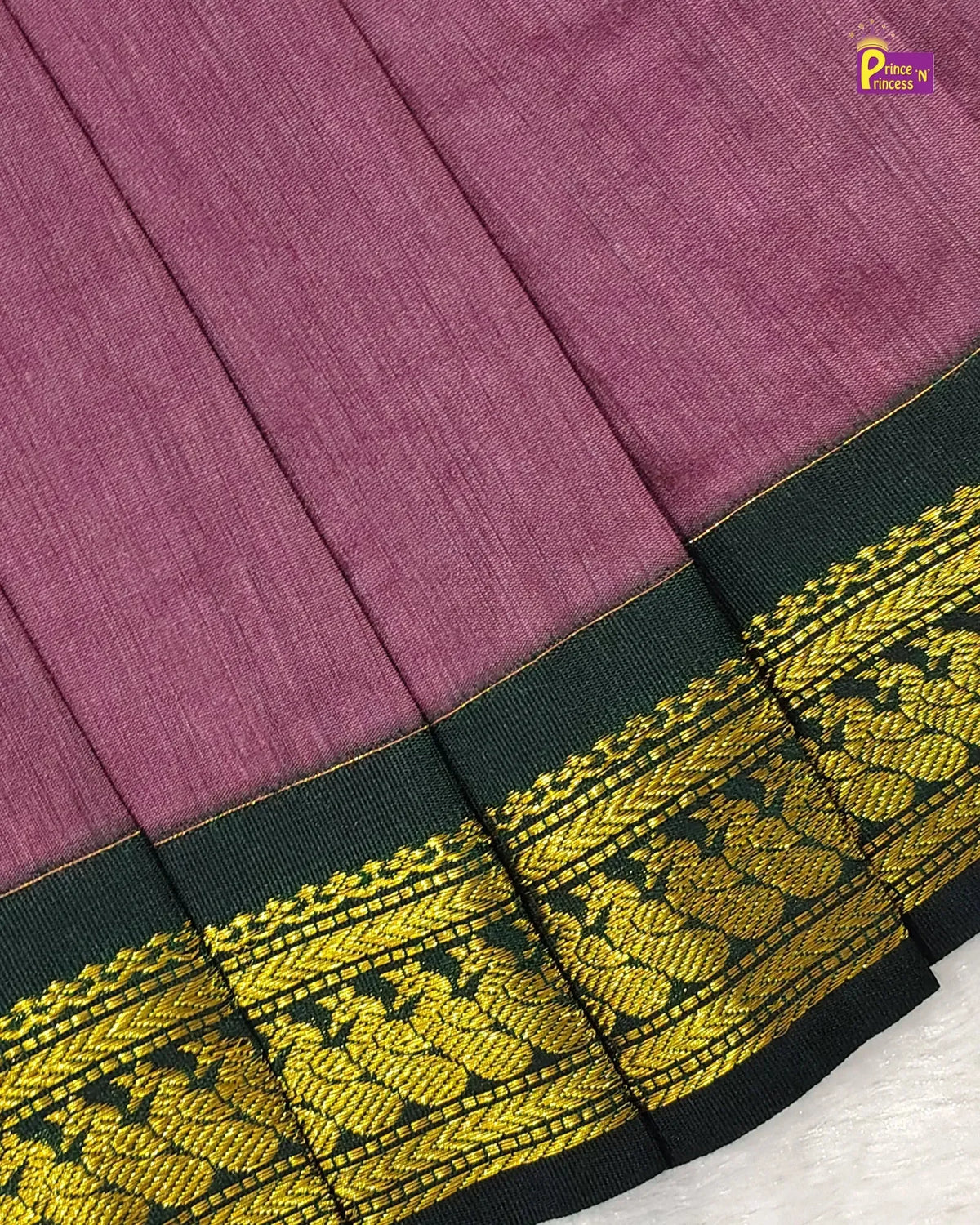 A close-up of a pleated fabric garment in dusty mauve-purple, featuring a wide black border with ornate gold woven detailing.